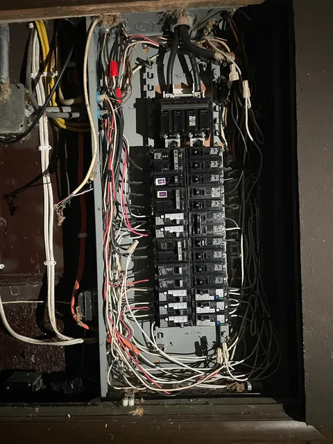 Old electrical panel with the cover removed, showing tangled wiring before replacement